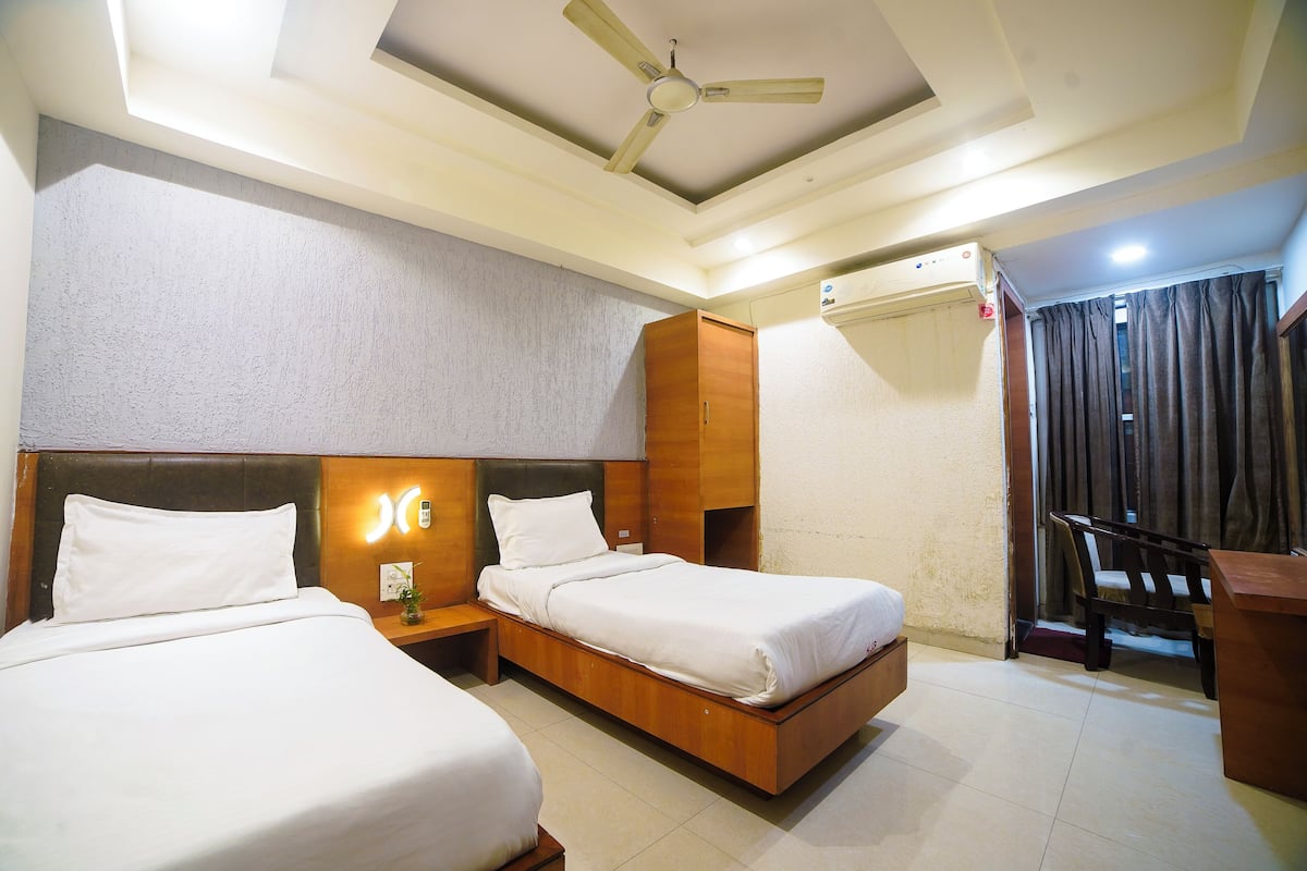 A hotel room with two beds, a ceiling fan, a bedside table with a lamp, and a window with curtains.