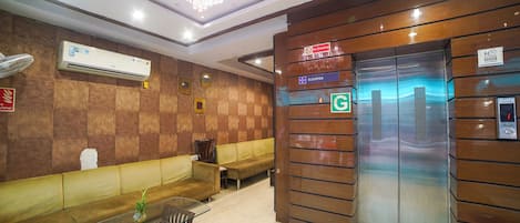 A lobby with a marble floor, a glass-top table, a sofa, an elevator, and a wall-mounted air conditioner.