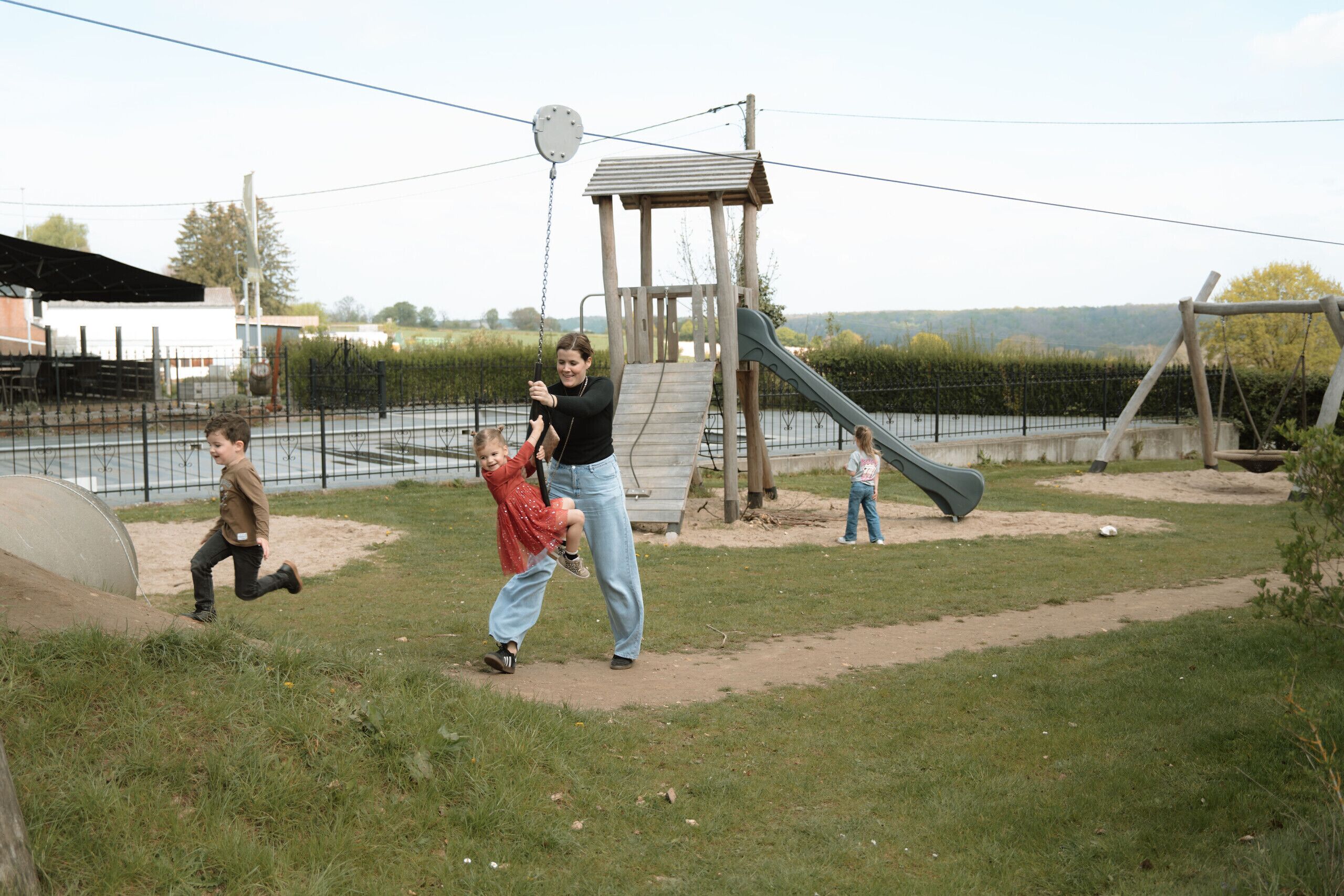 A playground with a slide and a climbing structure, surrounded by a fence and a body of water in the background.