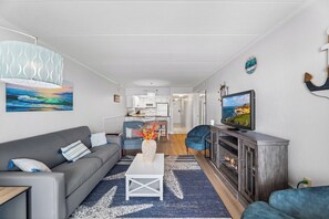 A modern living room with a grey sofa, a white coffee table, and a TV on a wooden cabinet. - Marigot Beach 403 2bedroom Oceanfront (Ocean City)