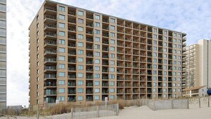 A high-rise building with multiple balconies and a sandy ground area in front. - Marigot Beach 403 2bedroom Oceanfront (Ocean City)
