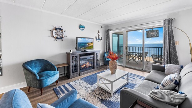 A modern living room with a fireplace, a television, and a balcony with a view of the sea. - Marigot Beach 403 2bedroom Oceanfront (Ocean City)