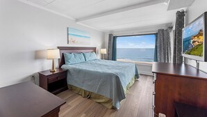 A bedroom with a bed, bedside tables, a TV, a window with a view of the sea, and a painting on the wall. - Marigot Beach 403 2bedroom Oceanfront (Ocean City)