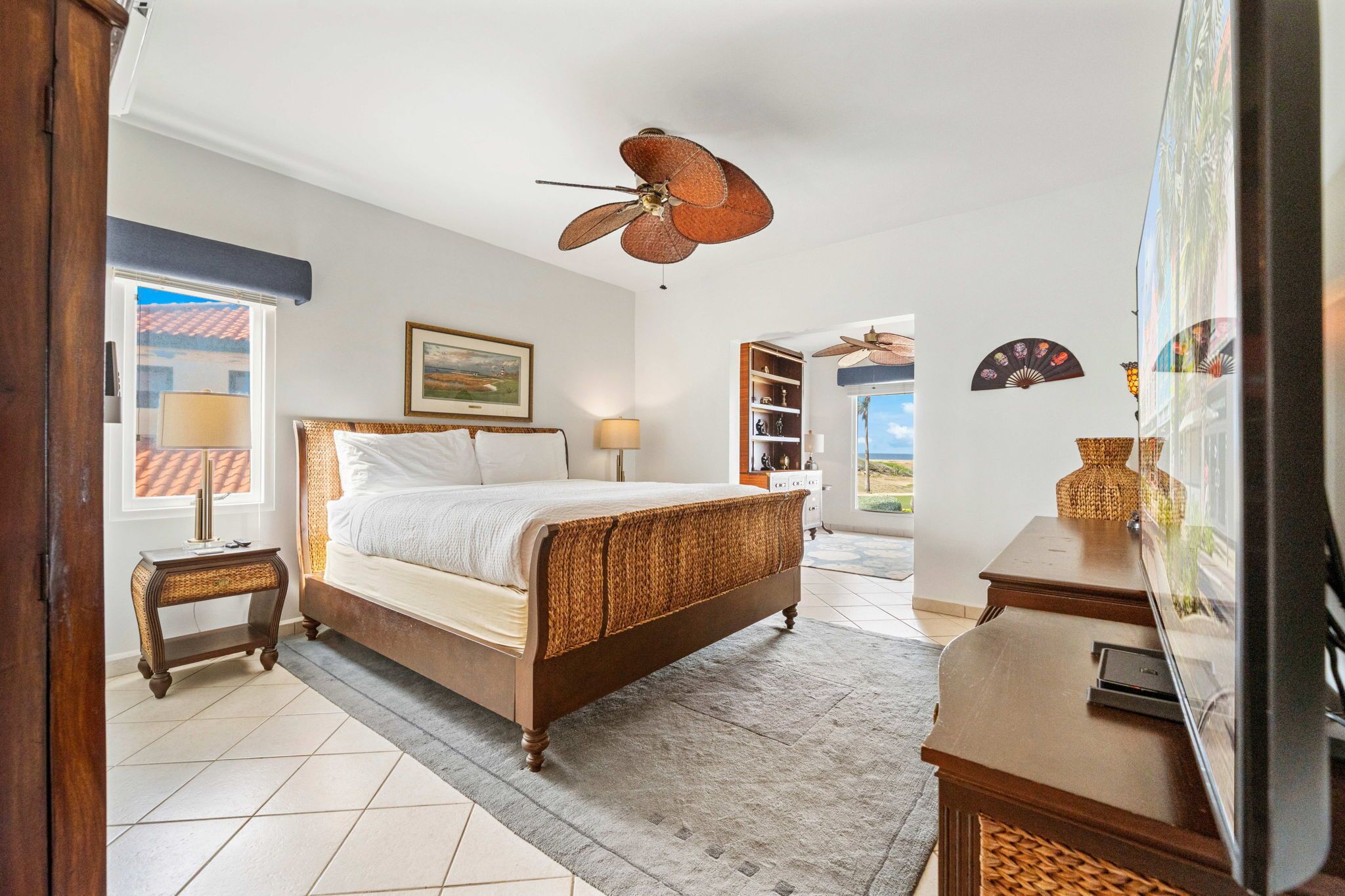 A bedroom with a bed, a ceiling fan, a TV, and a window with a view.