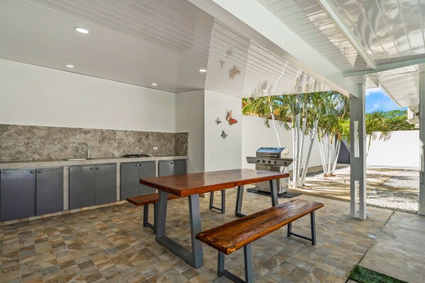 A modern kitchen with a wooden table and bench, a built-in grill, and a view of the beach. - Opal 24 (Noord)