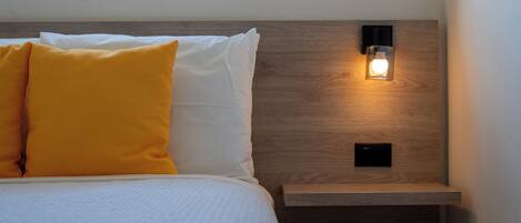 A neatly made bed with white and yellow pillows, a wooden headboard, and a bedside table with a wall-mounted light.