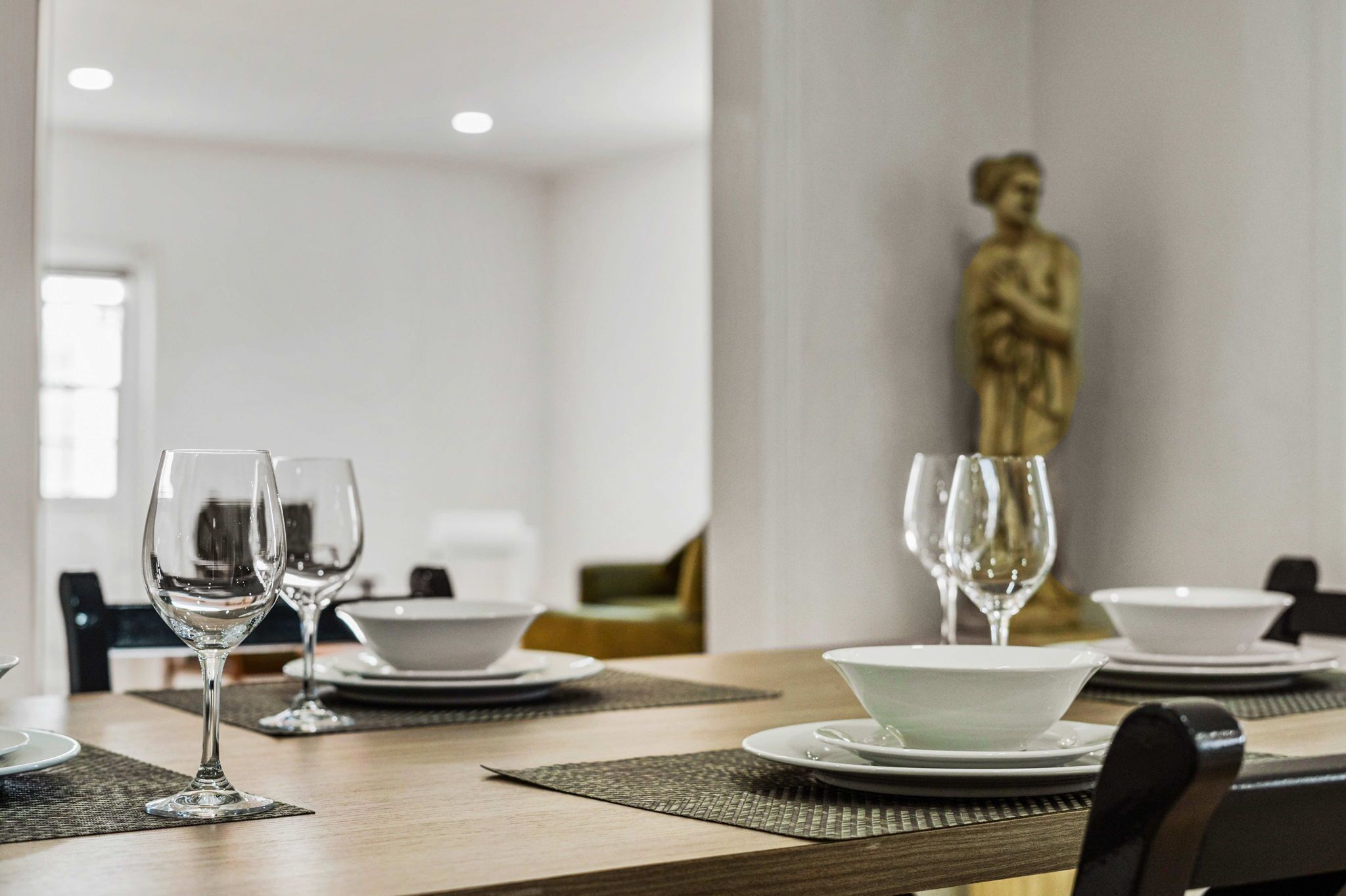 Une table à manger dressée avec des verres à vin, des bols et des assiettes, et une statue en arrière-plan.