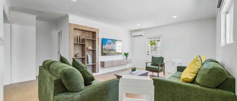 A modern living room with green sofas, a white coffee table, and a wooden shelving unit.