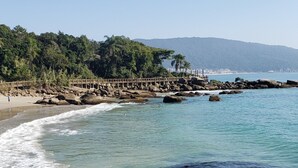 A beach with clear water, rocks, and a wooden walkway. - LM64 Lobster House in Bombinhas for 15 people Share Save (Bombinhas)