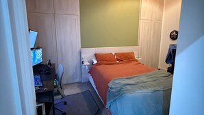 Un dormitori amb llit, escriptori amb ordinador i una cadira.