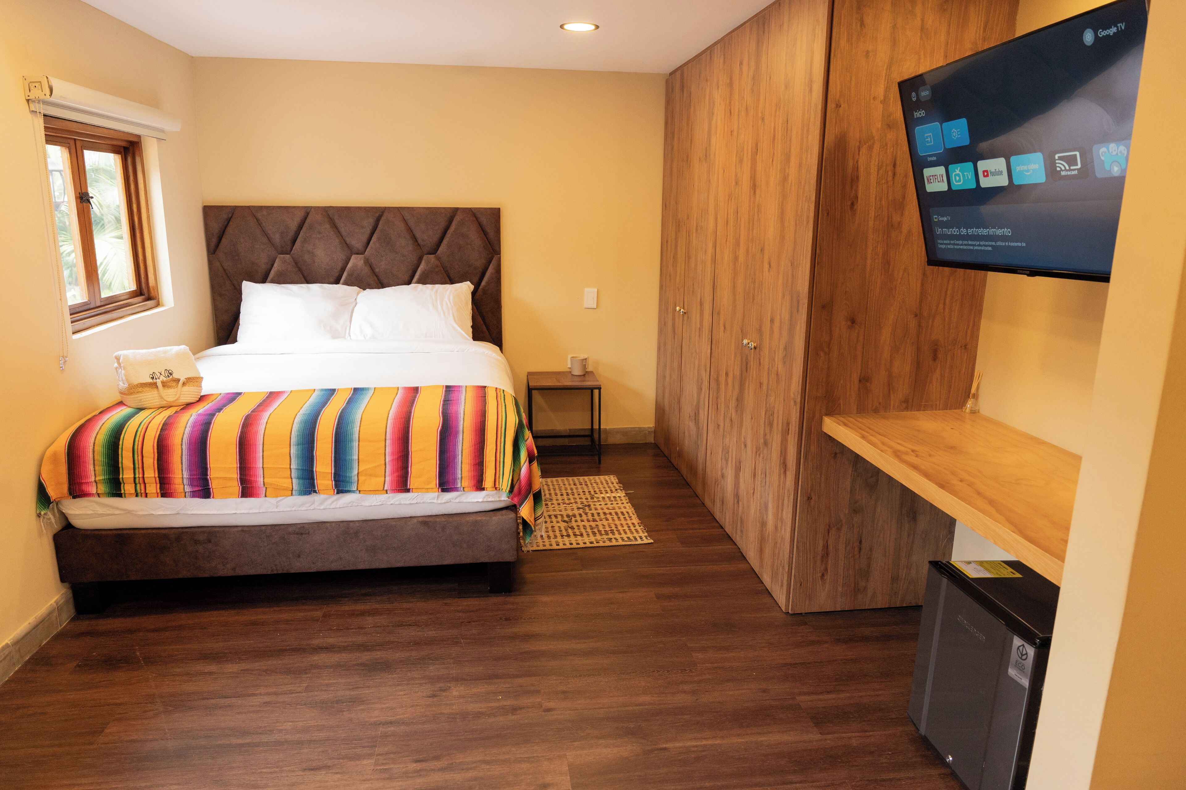 Une chambre d’hôtel avec un lit, une télévision, une armoire en bois et un petit bureau.