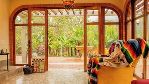 A room with a yellow armchair, a wooden bench, and a view of a garden through large arched windows. - Hotel Campestre Rancho La Lechería (Cali)