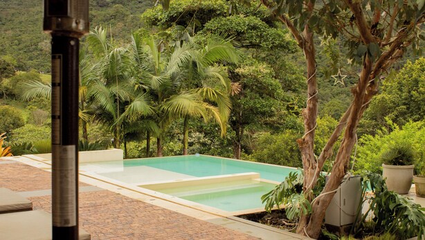 A rectangular swimming pool with a tiled deck, surrounded by lush greenery and palm trees. - Hotel Campestre Rancho La Lechería (Cali)