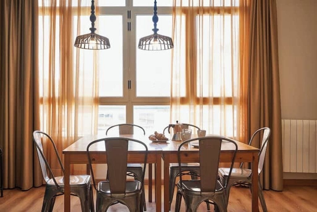 Un espace repas comprenant une table en bois, des chaises en métal et deux luminaires suspendus.