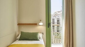 A bedroom with a bed, a nightstand, a lamp, and a view of a balcony with buildings.