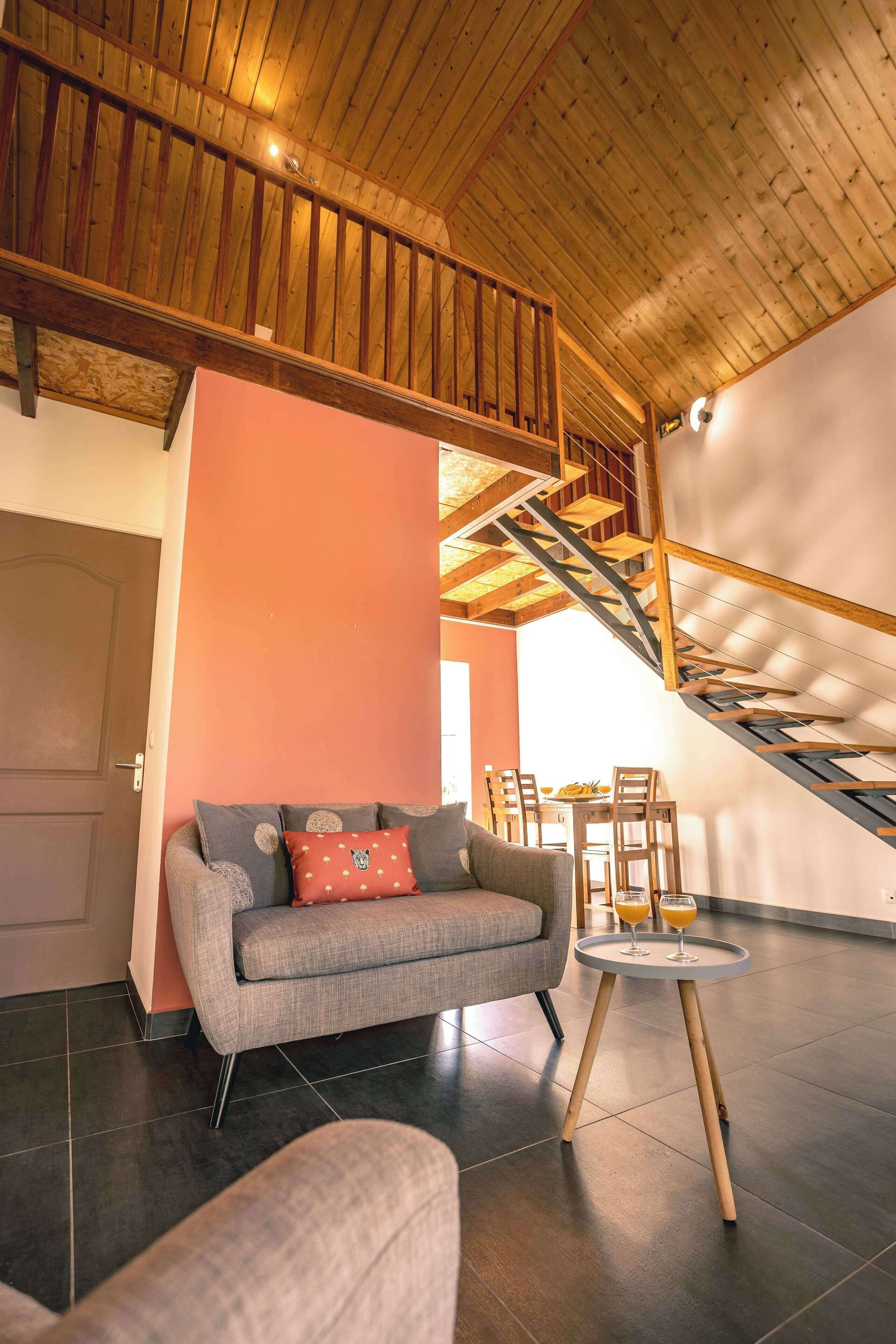 A modern living room with a grey sofa, a small round table with glasses, and a staircase with wooden railings.