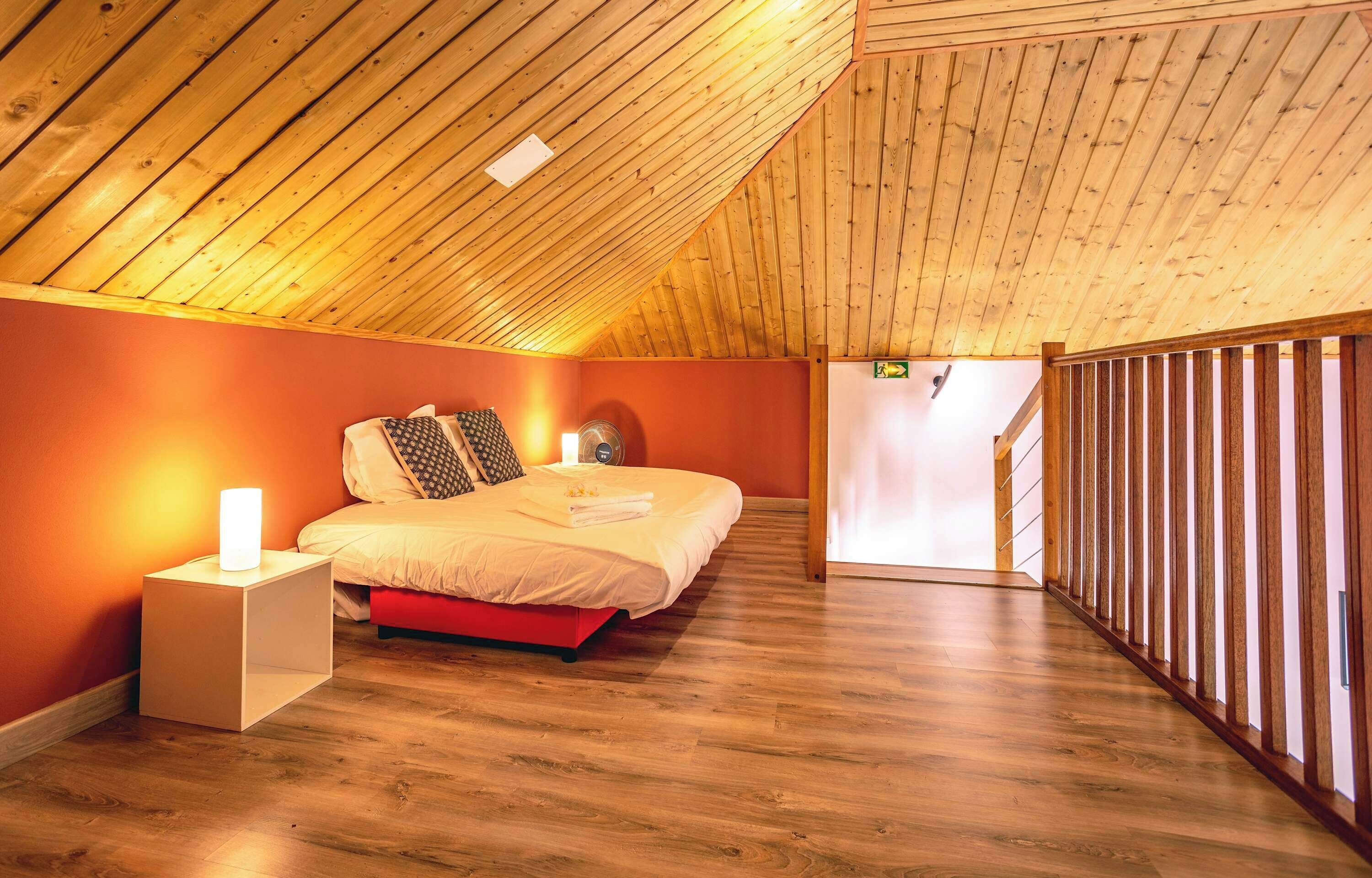 Een slaapkamer met een schuine kap, een bed met kussens, een nachtkastje met een lamp en een houten vloer.