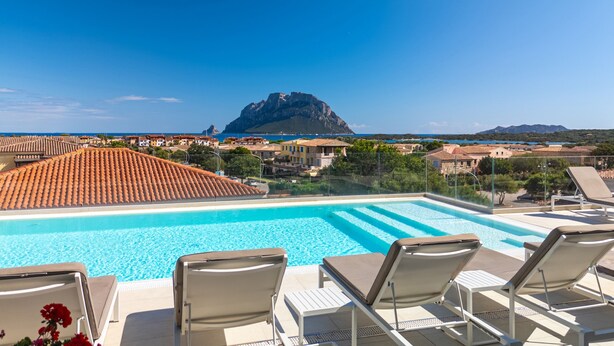 A swimming pool with lounge chairs, a mountain in the background, and a coastal town. - Residence with panoramic swimming pool in Porto San Paolo just 850 mt from the sea (Porto San Paolo)