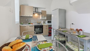 Une cuisine compacte dotée d’appareils électroménagers modernes, un coin repas avec une table dressée pour deux personnes et une vue sur la mer.