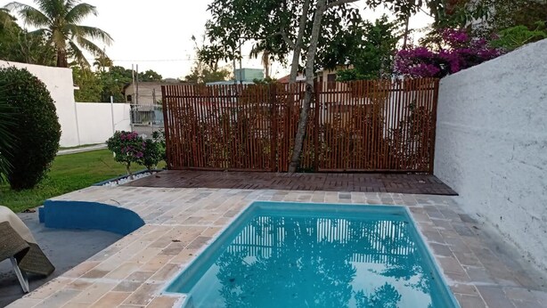 Une piscine rectangulaire, bordée d’une terrasse carrelée et entourée d’une clôture en bois et d’un mur blanc.