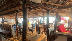 An outdoor dining area with wooden tables and chairs, a thatched roof, and a sandy floor. - Villa Maroloko (Ifaty)