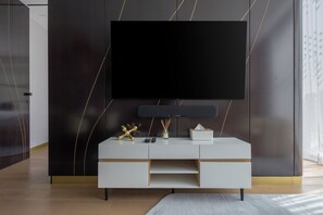 Ein modernes Wohnzimmer mit einem großen Flachbildfernseher an einer dunklen Wand, einem weißen Konsolentisch mit Schubladen und einem kleinen dekorativen Gegenstand auf dem Tisch.