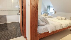 A bedroom with a wooden bed, a bathroom with a shower, and a view of the outside. - Bubbs Cottage (Dorchester)
