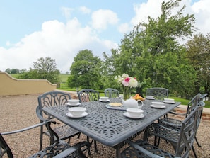 A table set outdoors with chairs, a vase of flowers, and a bowl of fruit. - Highfields Farm (Church Stretton)
