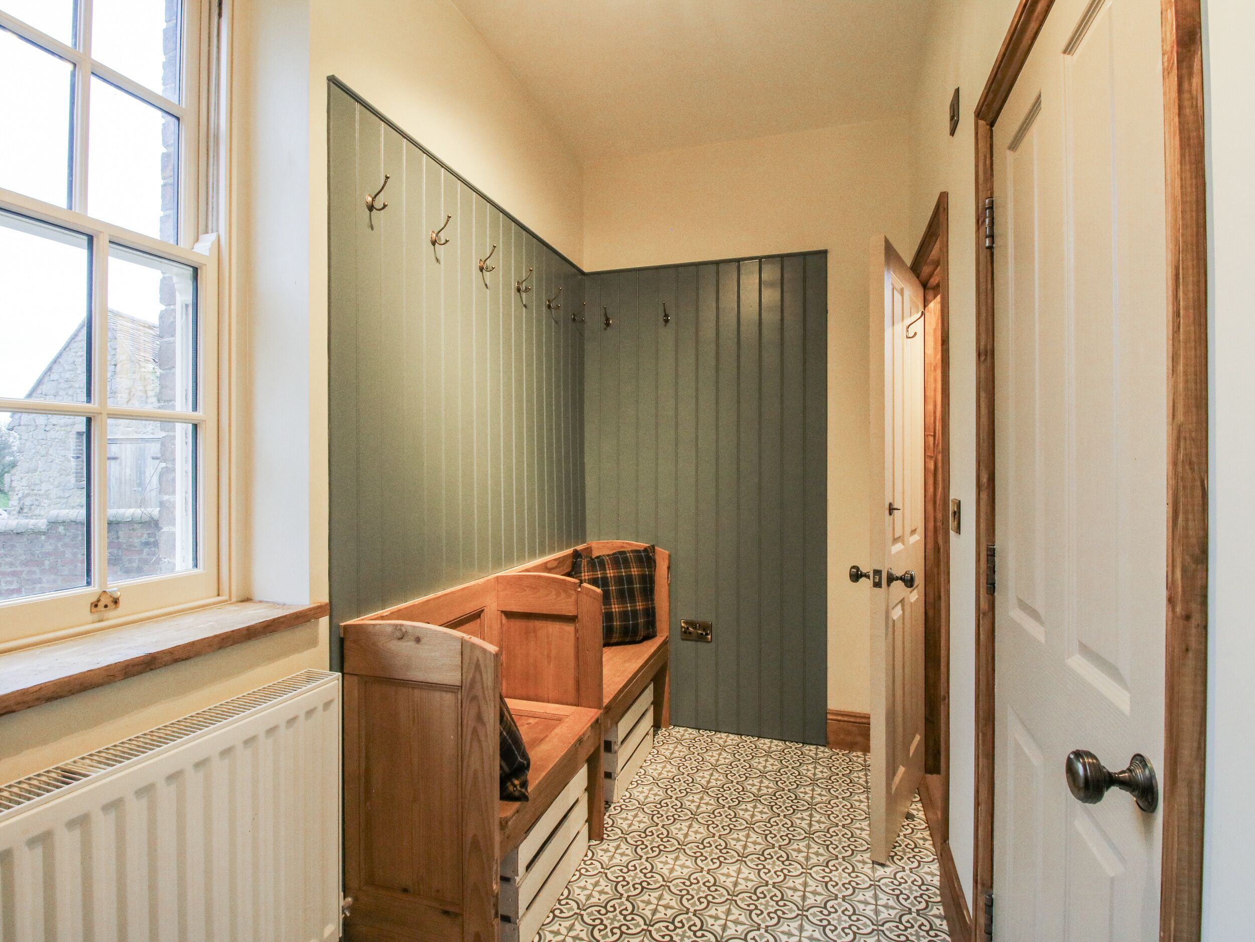 A narrow hallway with a wooden bench, a radiator, patterned floor tiles, and a door with a handle.