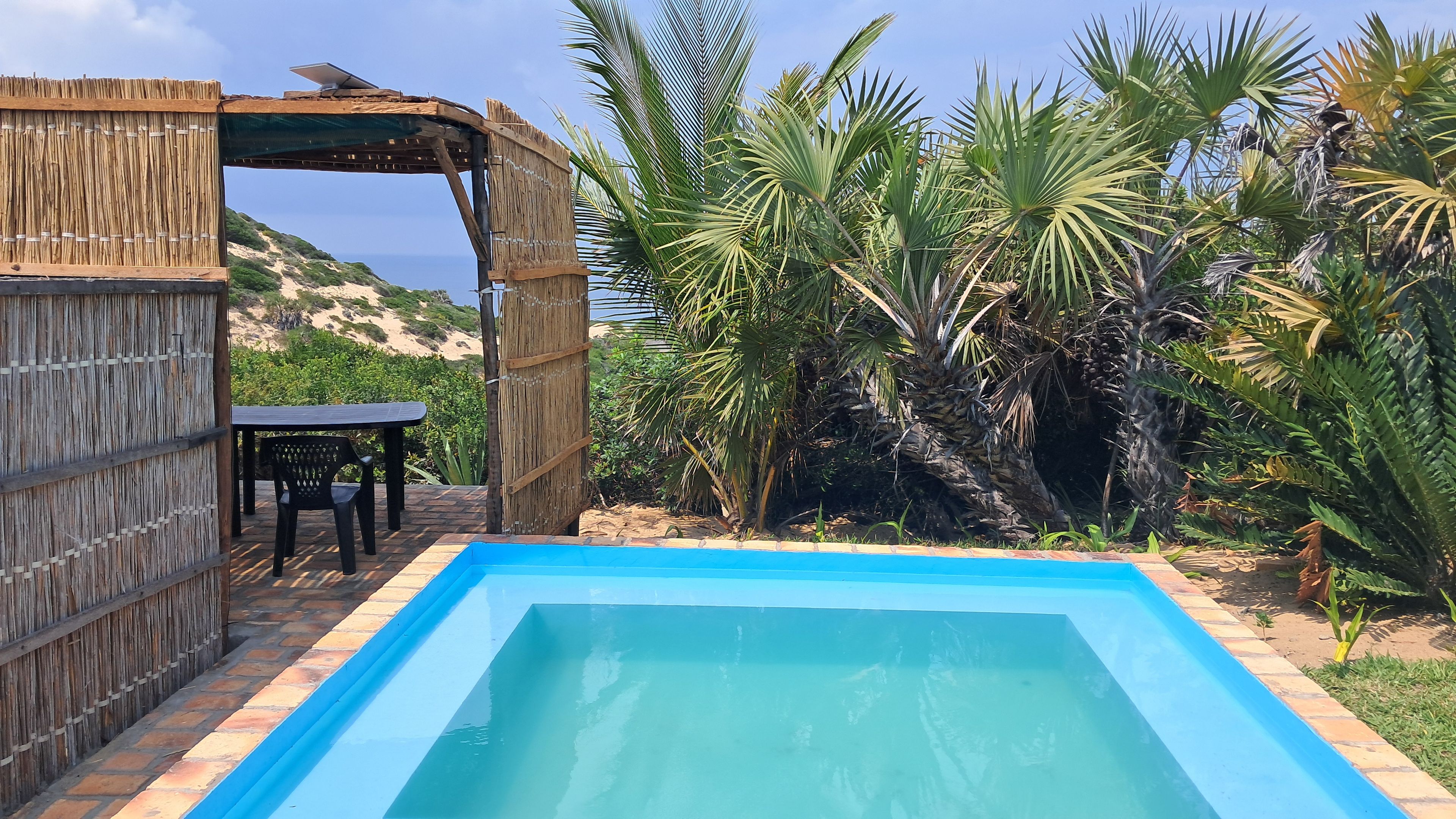 A swimming pool with a wooden pergola and a table and chairs nearby.