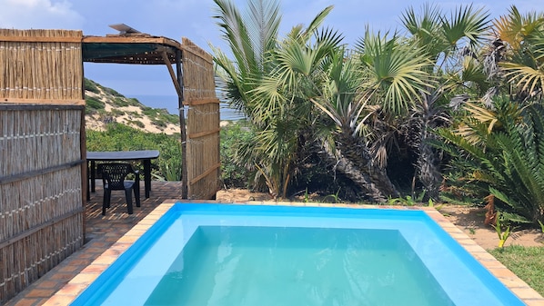 A swimming pool with a wooden pergola and a table and chairs nearby.