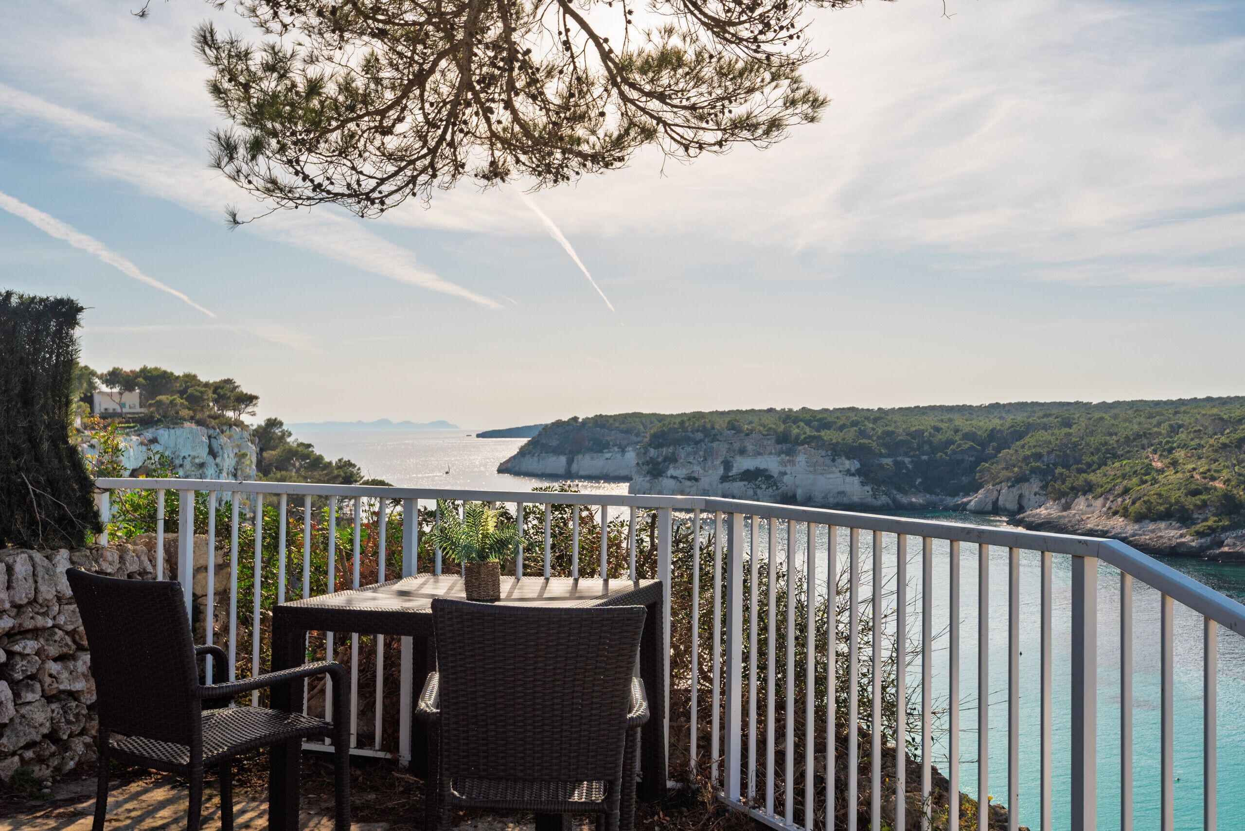 A balcony with wicker furniture overlooking a coastal landscape with cliffs and the sea.