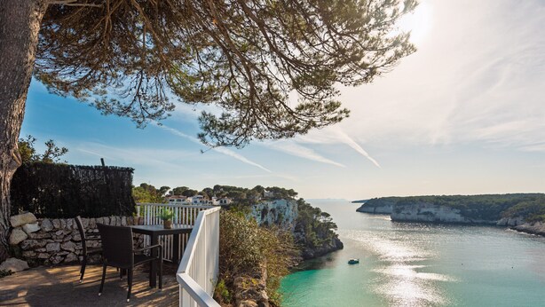 Ein Küsteneigentum mit einer Terrasse, Stühlen, einer Steinmauer und Blick auf das Meer und die Klippen.