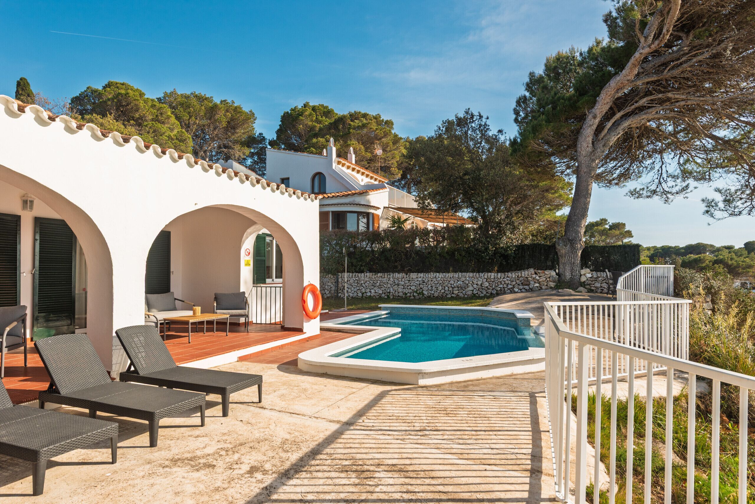 A pool area with lounge chairs, a stone wall, and a view of the surrounding landscape.