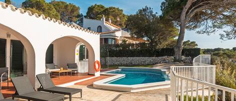 A pool area with lounge chairs, a stone wall, and a view of the surrounding landscape.