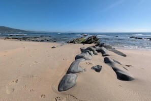 En strand med stora stenar i sanden och fotspår.