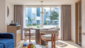 A modern hotel room with a large window, a round dining table, and a blue sofa. - Sterling Arka Suites Puri (Brahmagiri)