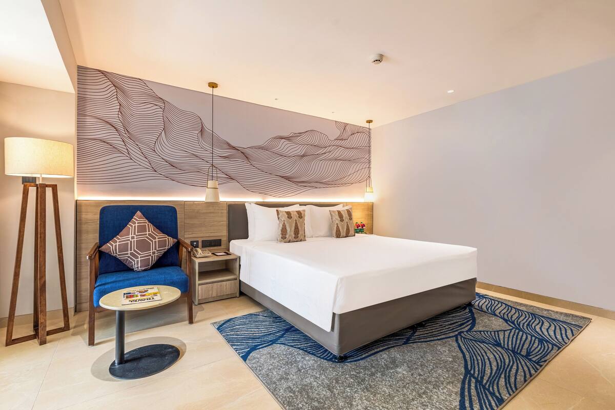 Une chambre d’hôtel moderne avec un grand lit, un fauteuil bleu, une petite table ronde et un élément décoratif mural.