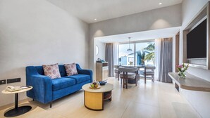 A modern living room with a blue sofa, a round coffee table, and a dining area with a table and chairs. - Sterling Arka Suites Puri (Brahmagiri)