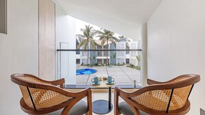 A balcony with two wooden chairs, a small table, and a view of a pool and buildings. - Sterling Arka Suites Puri (Brahmagiri)
