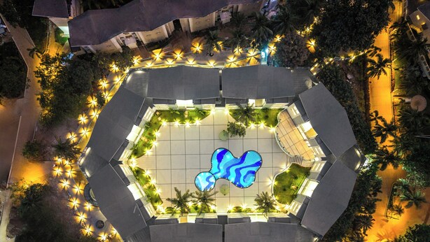 An aerial view of a hexagonal pool surrounded by a garden with palm trees, under a night sky. - Sterling Arka Suites Puri (Brahmagiri)