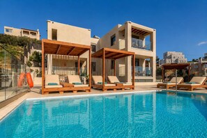 Uma área de piscina moderna com espreguiçadeiras e pérgulas de madeira, cercada por edifícios com varandas.