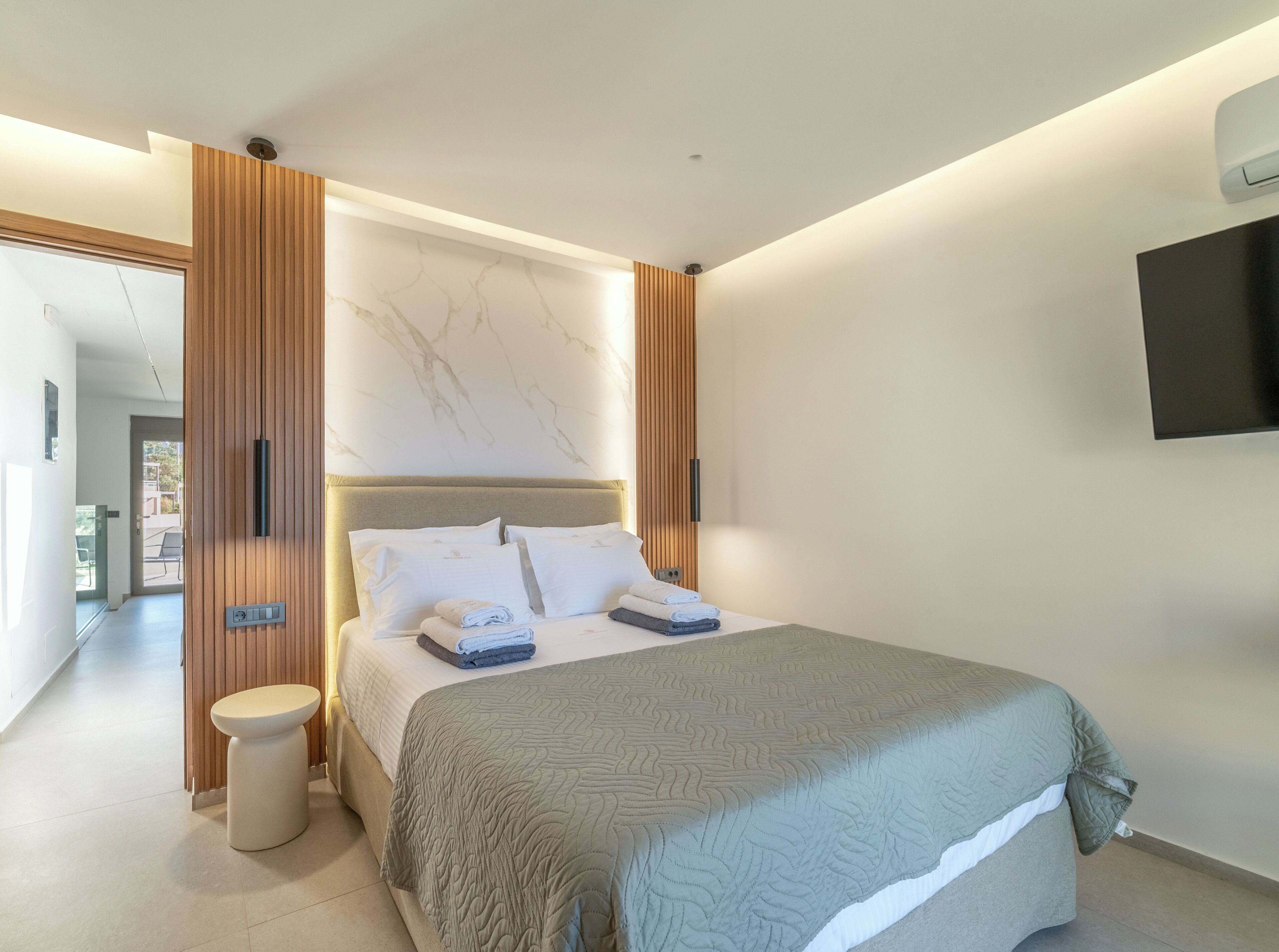 A modern bedroom with a bed, a bedside table, a wall-mounted TV, and a marble-patterned wall.