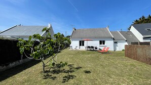 En bostadsfastighet med ett vitt hus, en liten uteplats med utemöbler och ett träd på gården.