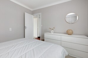 Ein Schlafzimmer mit einem Bett, einem Schminktisch, einem Spiegel und einer Vase mit getrockneten Blumen.