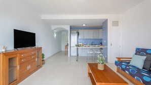 Sala de estar con televisor, muebles de madera, un sofá y una cocina al fondo.