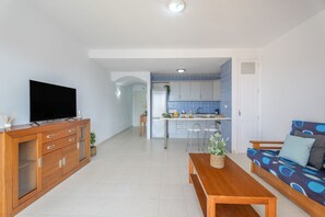 Een woonkamer met een televisie, houten meubels, een bank en een keuken op de achtergrond.