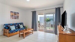 Una sala de estar con sofá, mesa de centro, televisión y balcón con mesa y sillas.