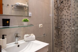 Une salle de bain avec une étagère en verre, un lavabo, un miroir, un porte-serviettes et un espace douche.