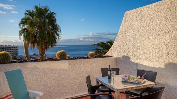 Una terraza con mesa puesta para comer, sillas, un cactus y vista al océano.